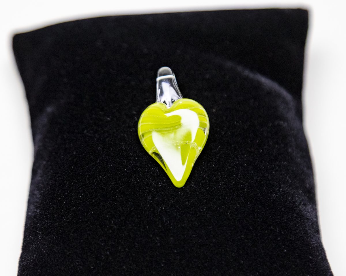A green and white glass heart pendant on a black velvet pillow
